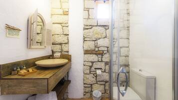 Un baño con pared de piedra, tocador de madera y cabina de ducha con vidrio.