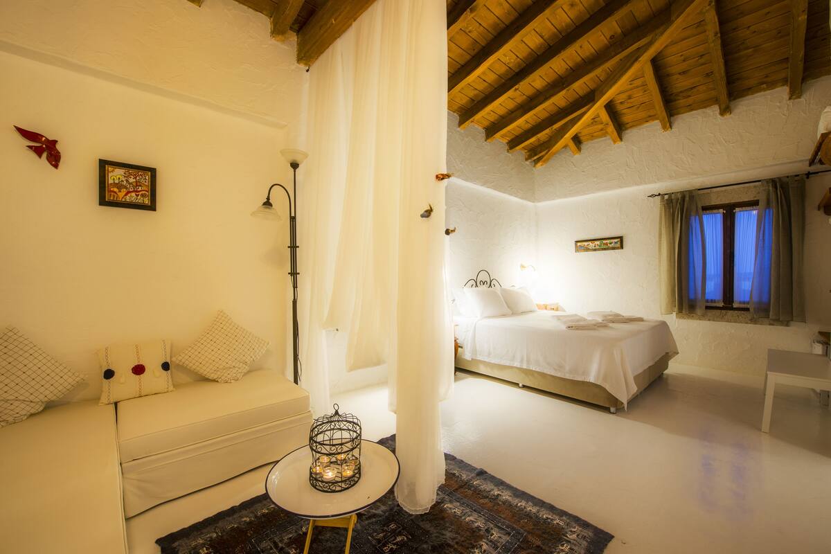 Un dormitorio con cama, mesita de noche, lámpara y ventana con cortinas.