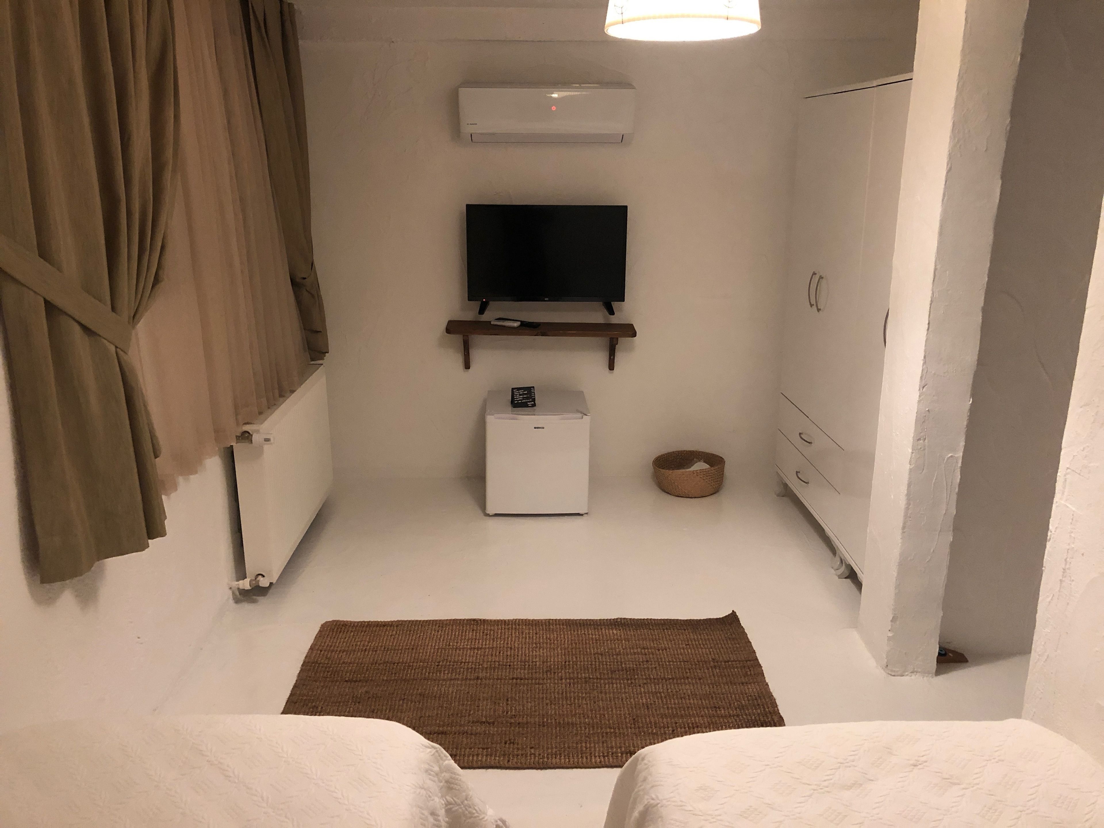 A small, clean room with a bed, a TV, a small fridge, and a basket.