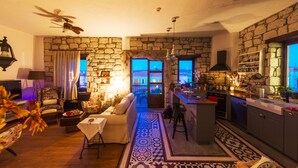 A cozy living room with a stone wall, a fireplace, and a view of the cityscape at dusk. - Jakamar Alacati (Cesme)