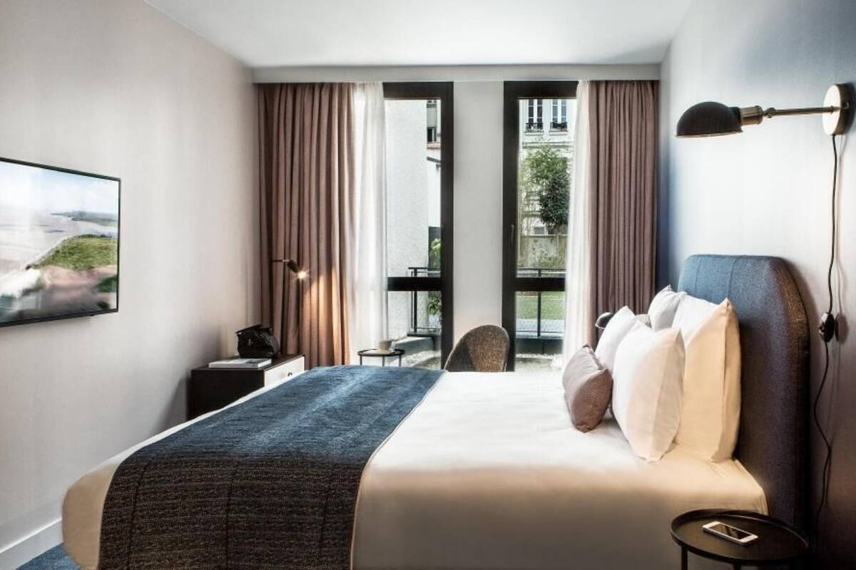 A hotel room with a bed, a desk, a chair, a TV, and a window with curtains.