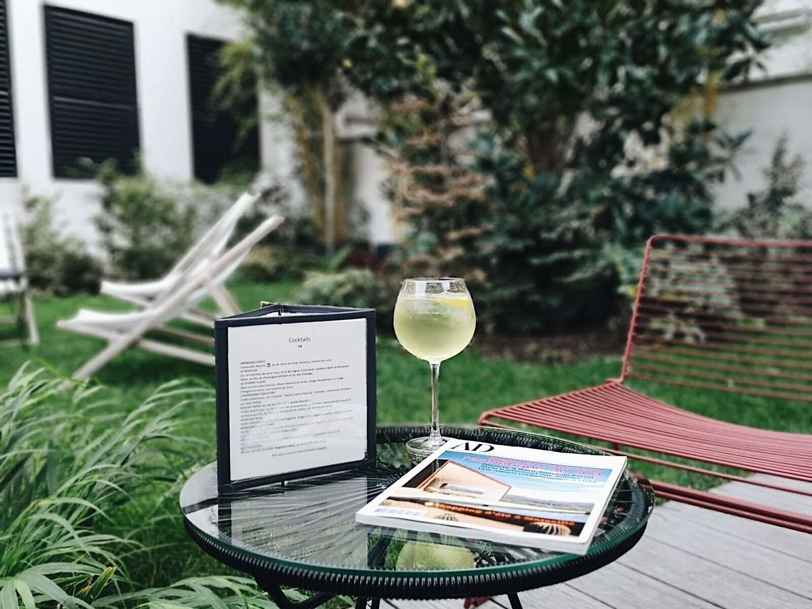 A glass of white wine on a glass table with a menu and a magazine.