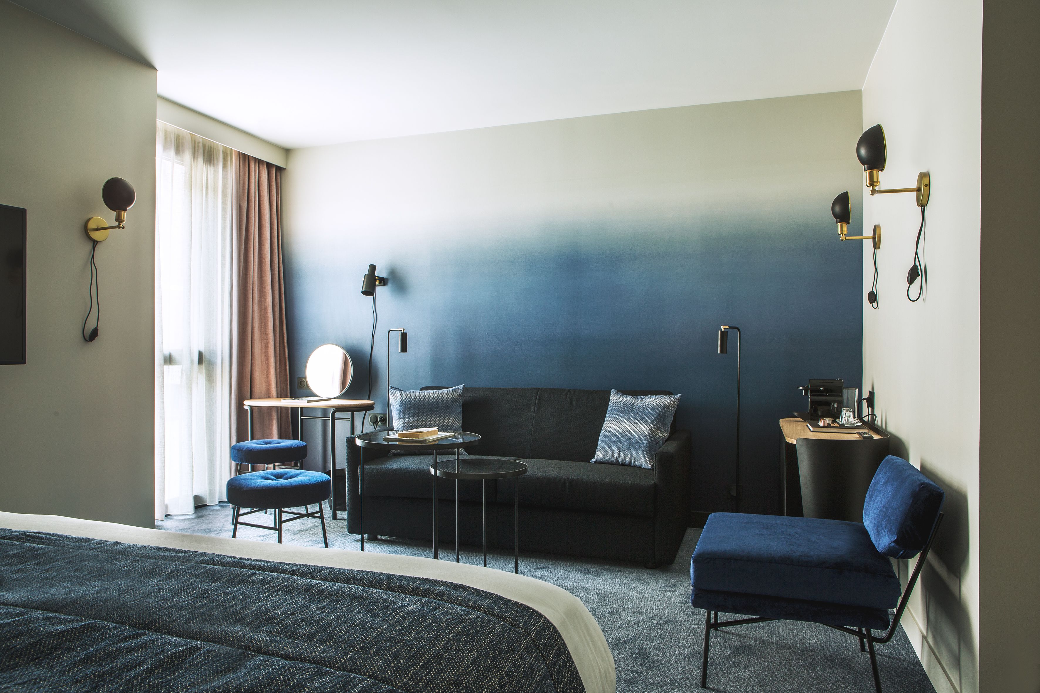 A modern hotel room with a bed, a sofa, a desk, and a chair.