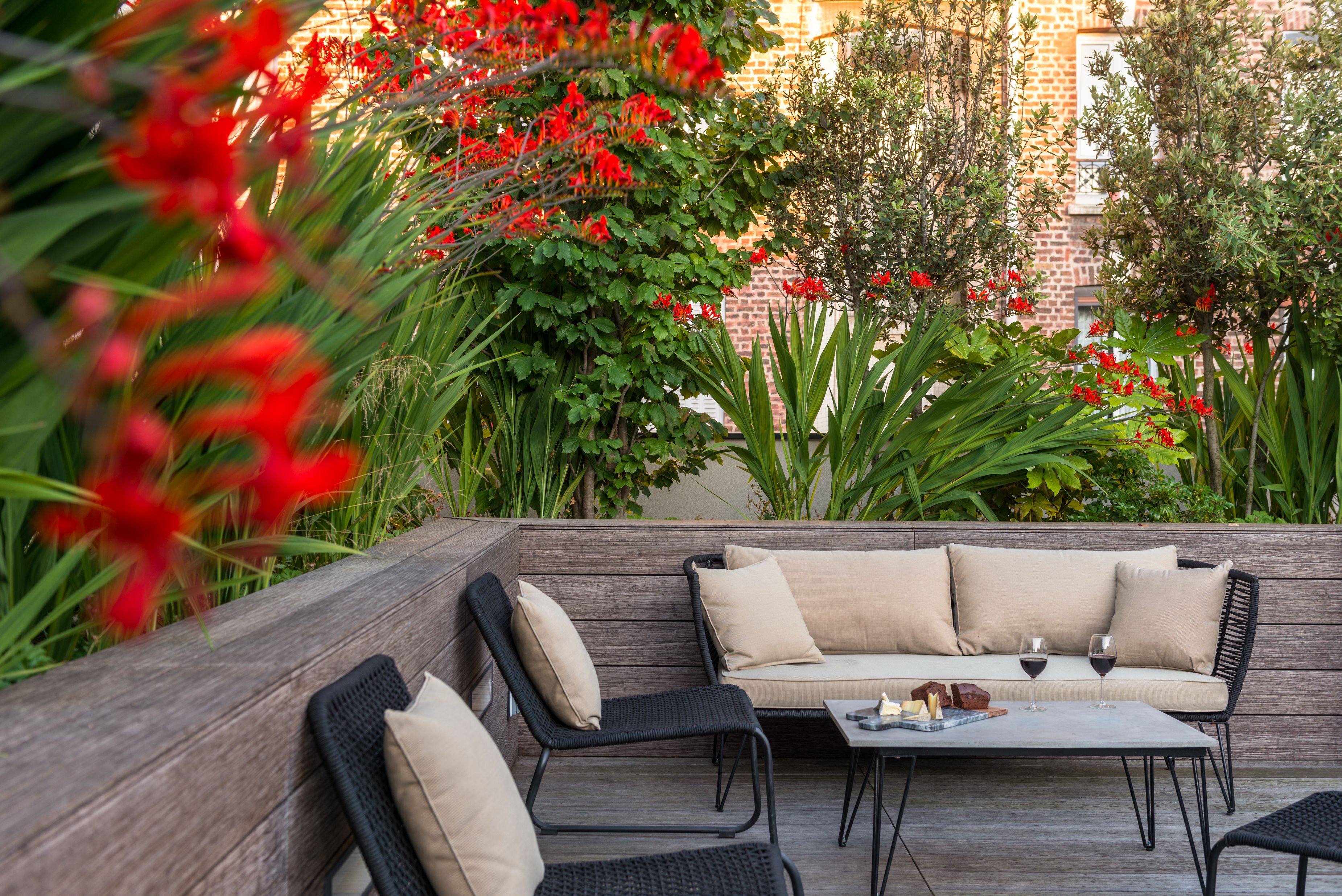 An outdoor seating area with a sofa and chairs, a table with wine glasses, and lush greenery.