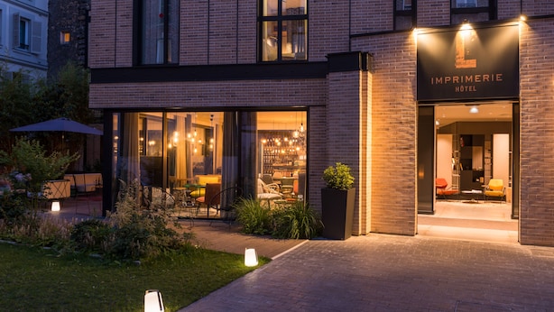 Exterior moderno de hotel, com entrada bem iluminada, área de estar ao ar livre e iluminação interior visível.