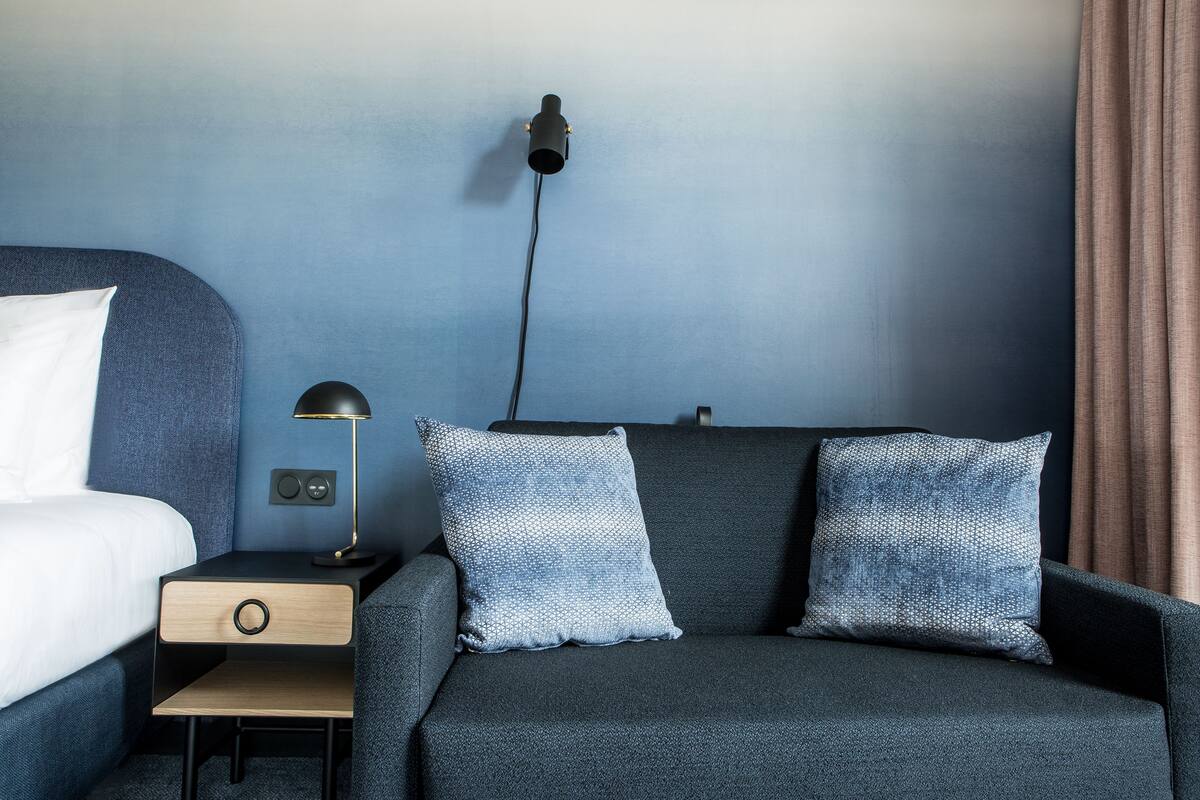 A modern hotel room with a bed, a nightstand, a lamp, and two patterned pillows.