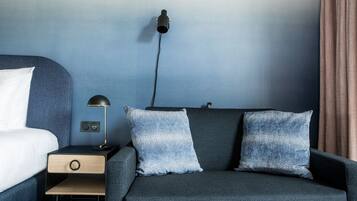 Una habitación de hotel moderna con una cama, una mesita de noche, una lámpara y dos almohadas estampadas.