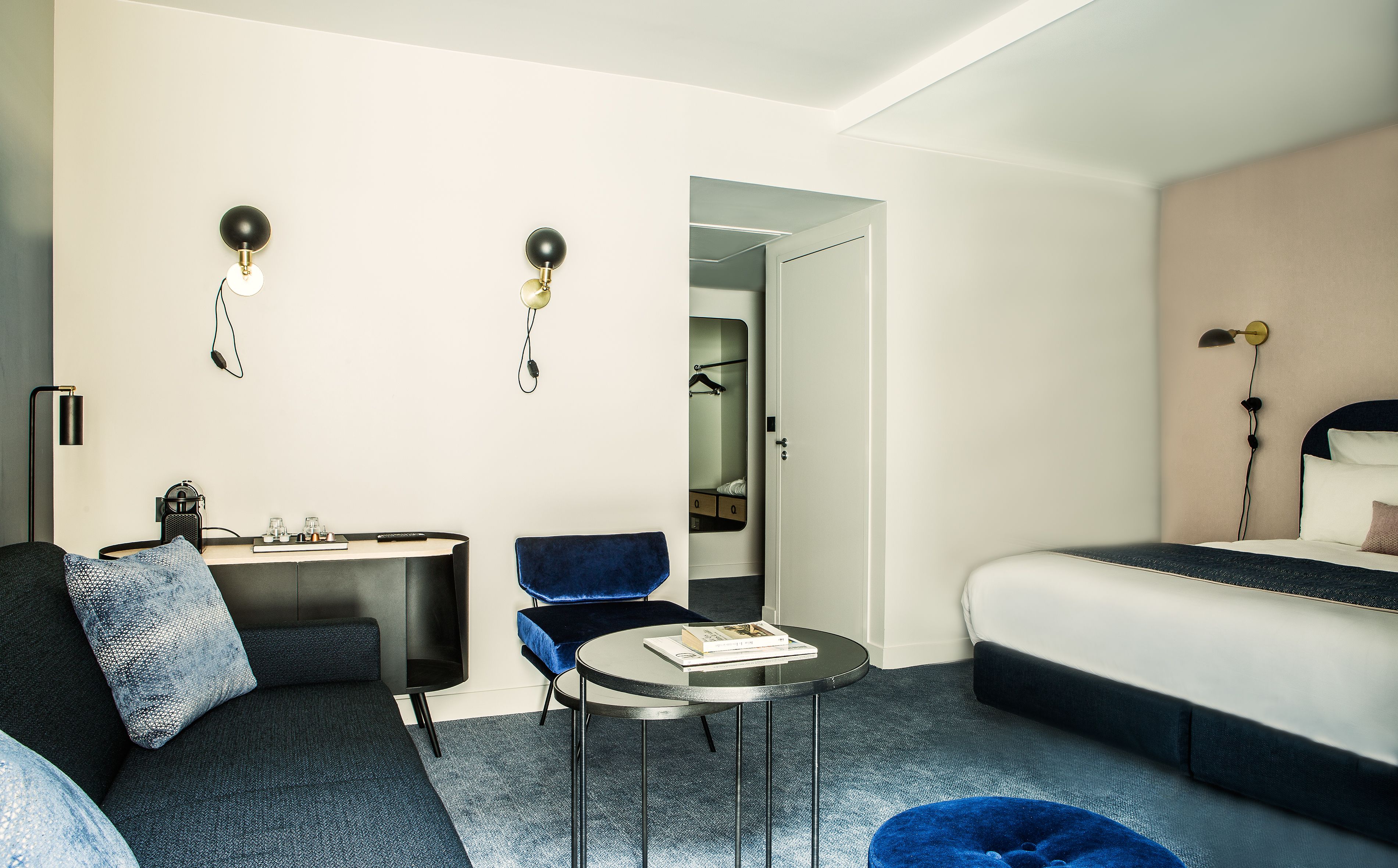 A hotel room with a bed, a desk, two chairs, a round table, and a mirror.