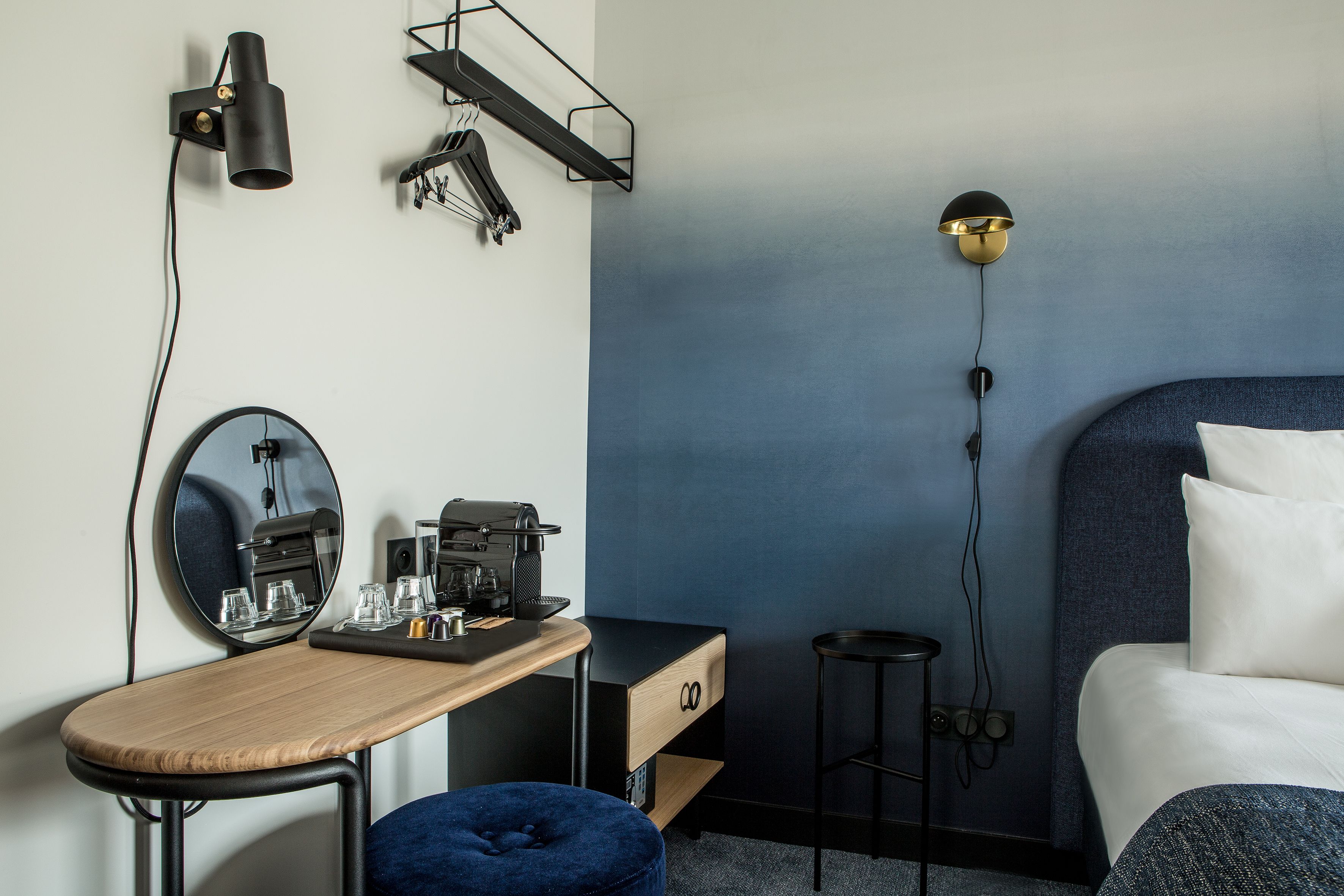 A modern hotel room with a desk, a bed, and a blue accent wall.