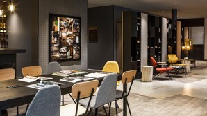 Uma sala de jantar moderna com uma mesa comprida, várias cadeiras e uma estante repleta de livros e objetos decorativos.