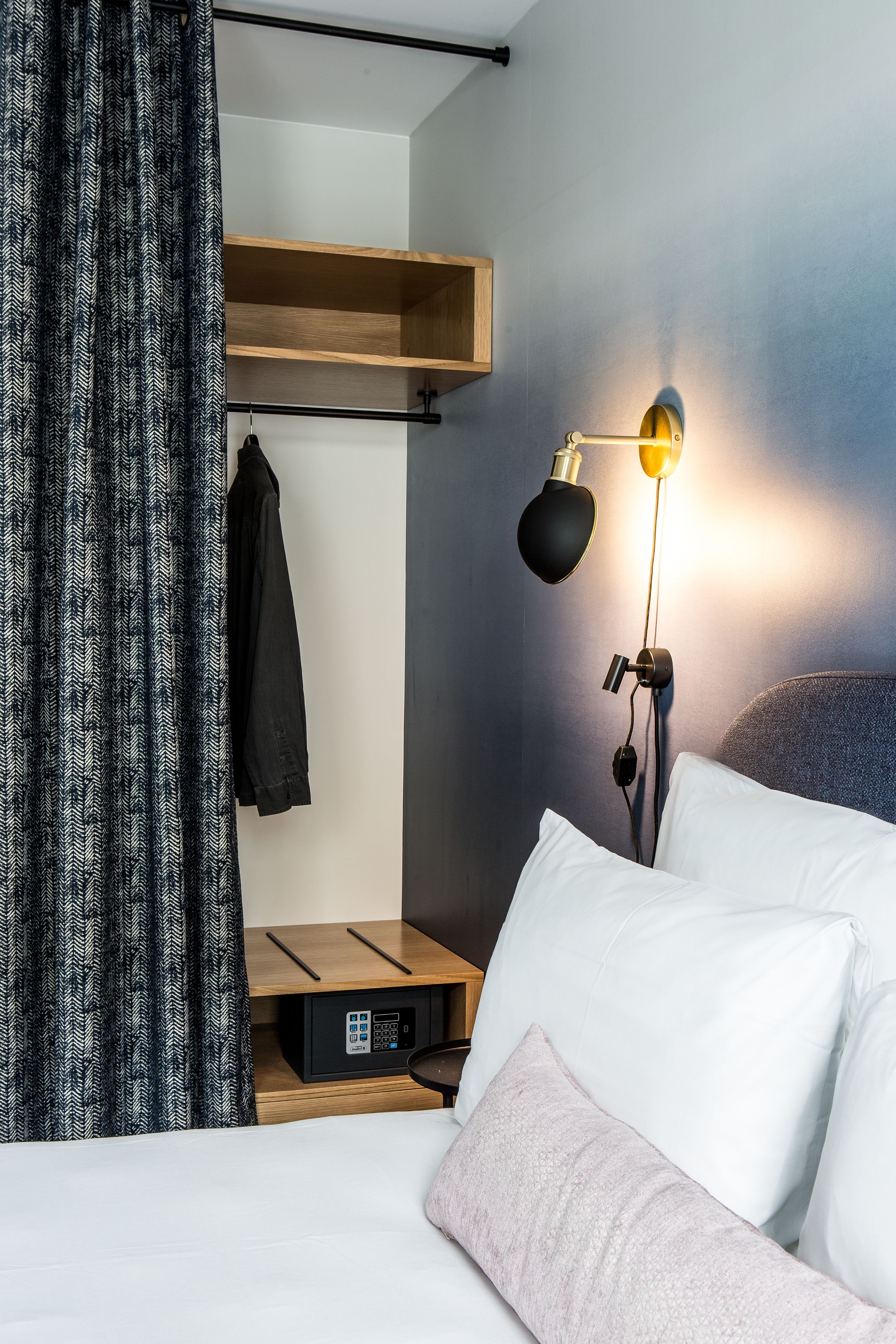 Een hotelkamer met een bed, een bedlamp, een kapstok en een houten plank.