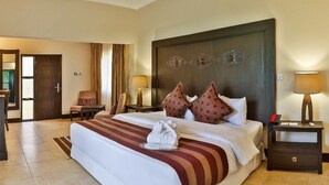 A hotel room with a large bed, a desk, a chair, and a nightstand with a lamp.