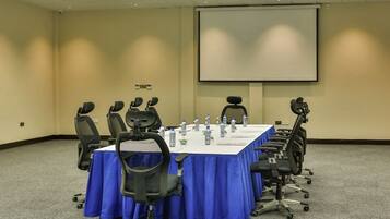 Un salón de conferencias con una larga mesa, varias sillas y una pantalla para proyector.