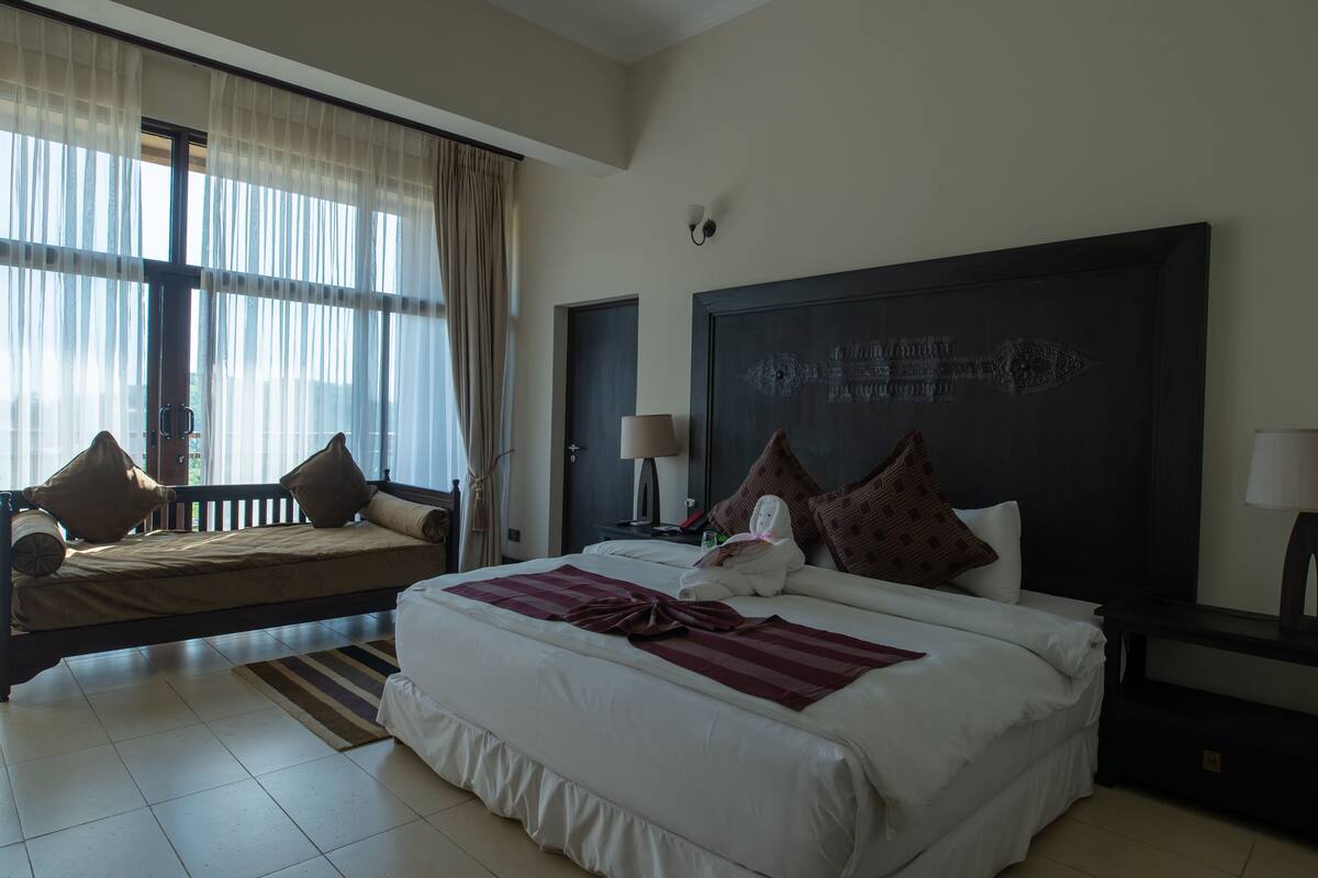 A hotel room with a large bed, a sofa, a desk, and a window with curtains.