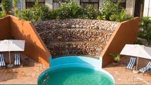 Una piscina con pared de piedra y sillones de descanso.
