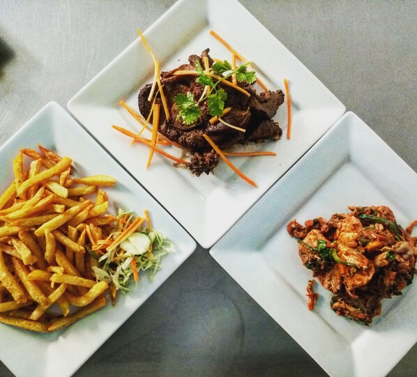 Tres platos cuadrados con diferentes comidas: uno con papas fritas, uno con carne, y uno con un guiso de verduras y carne.