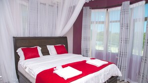Una cama bien tendida con ropa de cama blanca y roja, un cabecero de madera y cortinas de gasa.