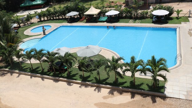 Una piscina grande con un borde arenoso, palmeras y sombrillas.