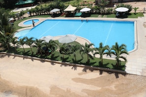 Una piscina grande con un borde arenoso, palmeras y sombrillas.