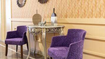 Un couloir avec un papier peint à motifs, un miroir rond doté d’un cadre en forme de soleil, et deux fauteuils violets recouverts d’un tissu à motifs floraux.