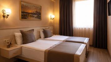 Quarto de hotel com duas camas, um quadro na parede e uma janela com cortinas.
