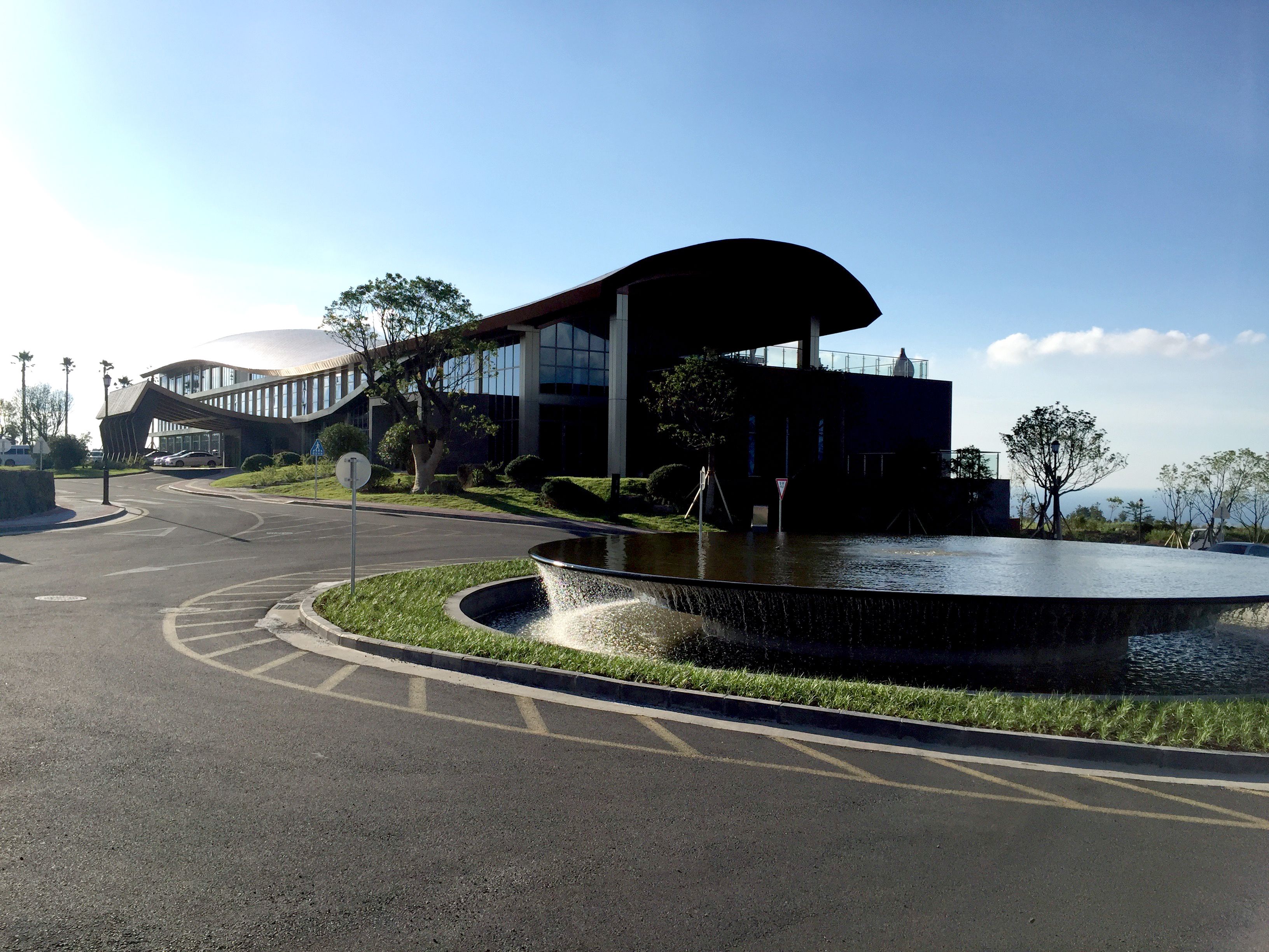 A modern building with a curved roof and a fountain in the foreground.