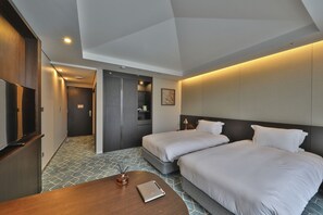 Quarto de hotel com duas camas, uma escrivaninha, uma televisão e uma porta para o banheiro.