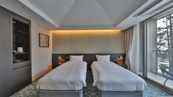 A hotel room with two beds, a built-in wardrobe, bedside lamps, and a large window with a view of the outdoors.