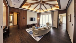 A spacious living room with a high ceiling, wooden beams, a large sofa, a flat-screen TV, and a dining area with chairs. - Camphortree Hotel & Resort (Jeju City)