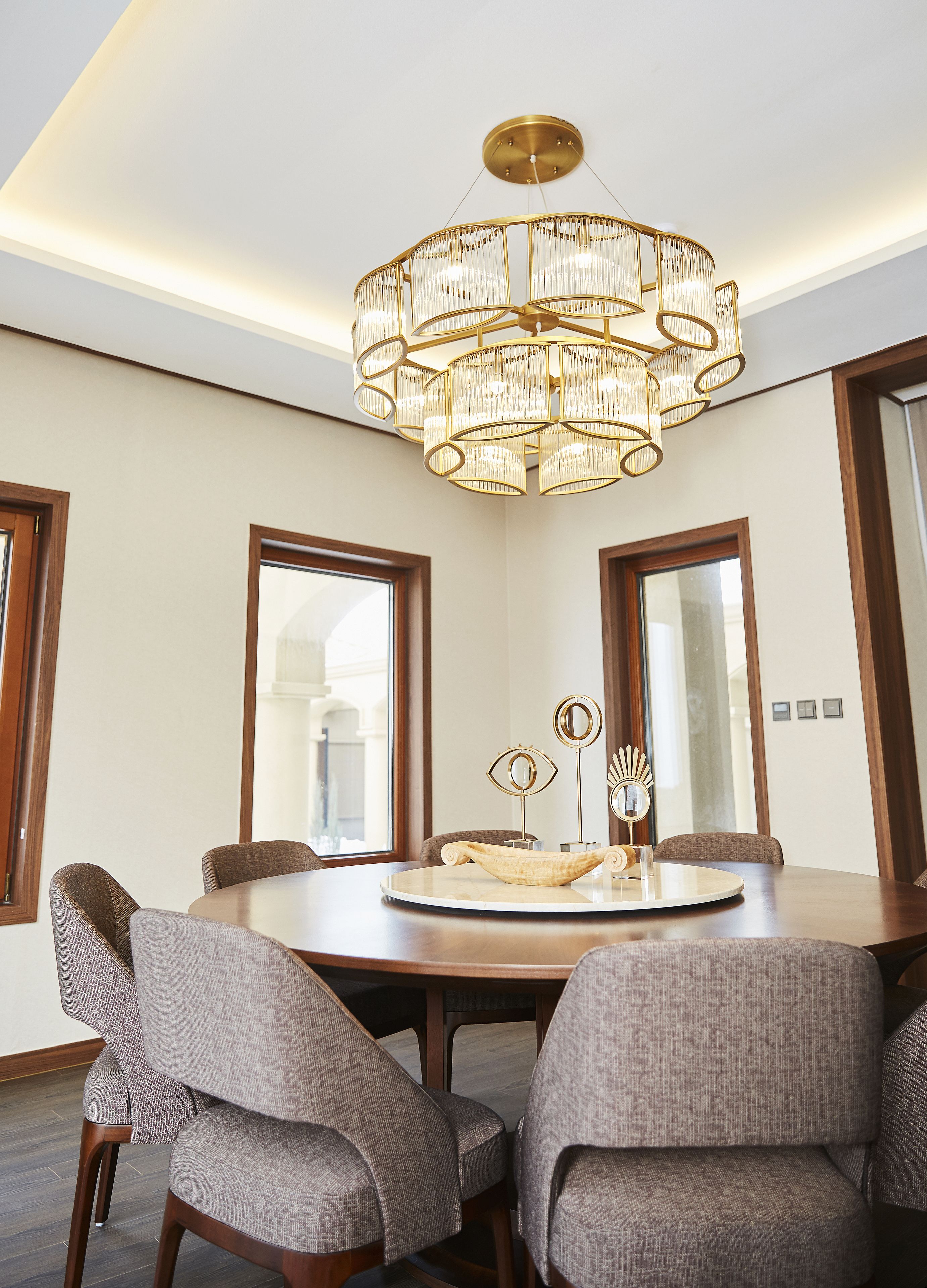 A dining area with a round table, six upholstered chairs, a chandelier, and two wall-mounted mirrors.