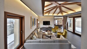 A modern living room with a sofa, coffee table, and yellow chairs. A flat-screen TV is mounted on the wall, and there is a dining area visible in the background. - Camphortree Hotel & Resort (Jeju City)