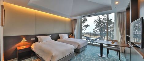 A hotel room with two beds, a dining table, a TV, and a balcony with a view.