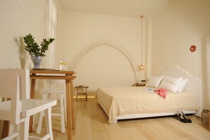 A bedroom with a bed, a desk, a chair, a small table, and a potted plant. - Veranda Rossa Suites (Rethymno)