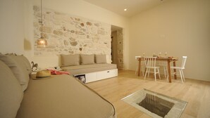 A cozy living room with a sofa, a dining table with chairs, a stone wall, and a hanging light fixture. - Veranda Rossa Suites (Rethymno)