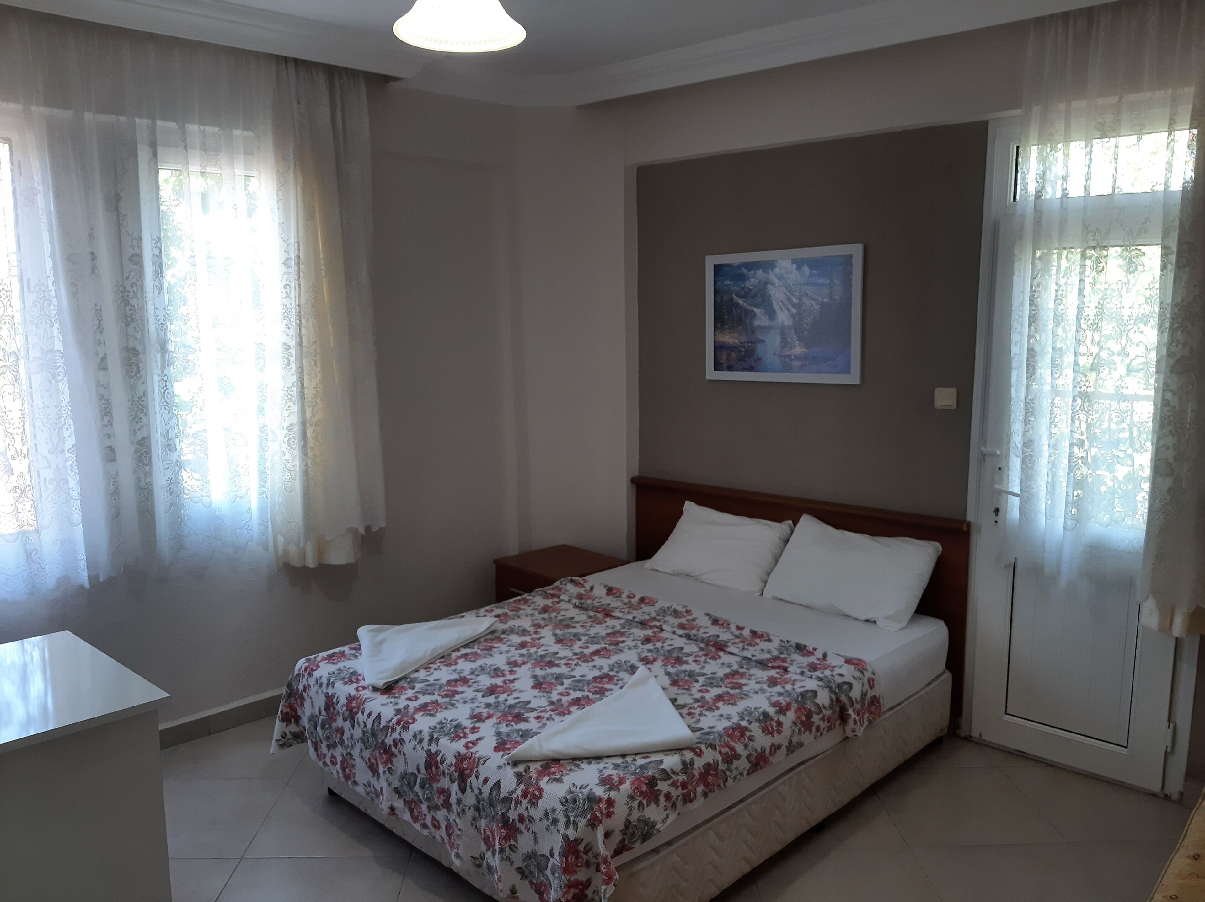 A bedroom with a bed, curtains, a painting, and a bedside table.