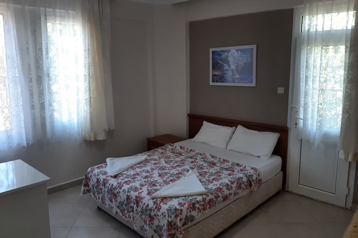A bedroom with a bed, curtains, a painting, and a bedside table.