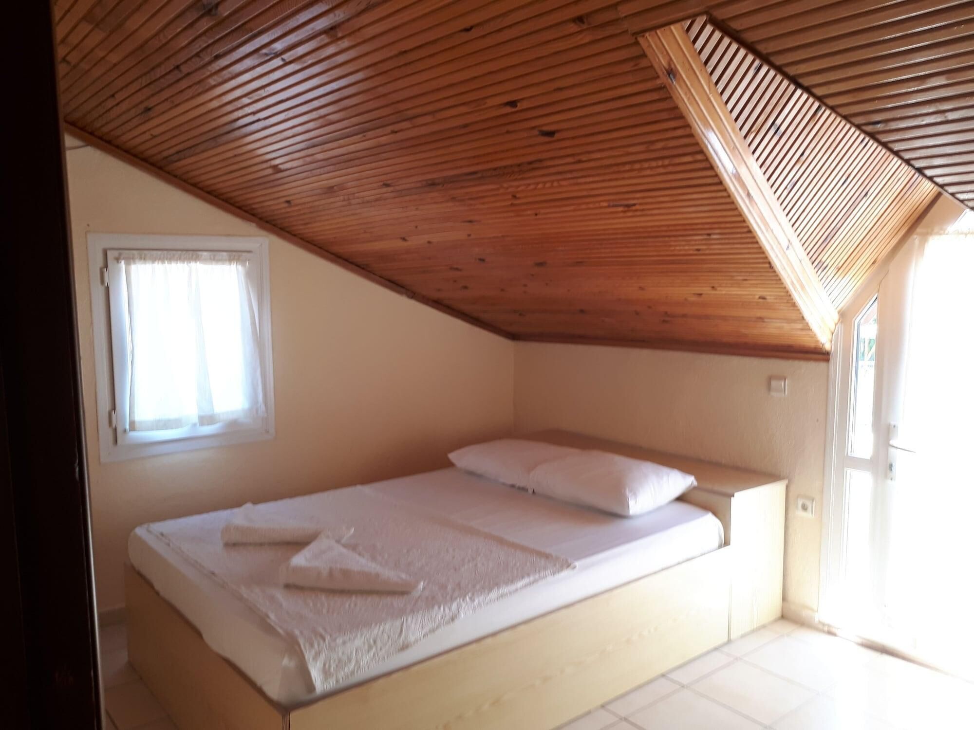 A small, single-bed room with a sloped ceiling and a window.