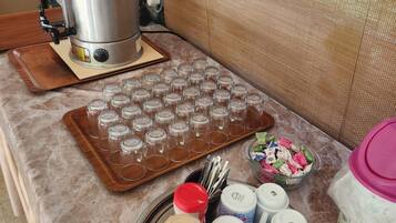 A kitchen counter with a coffee maker, a tray of empty glasses, a jar of coffee, a mug, and a bowl of snacks.