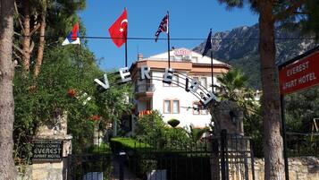 The entrance to Everest Apart Hotel with flags, a stone sign, and a view of the mountains.