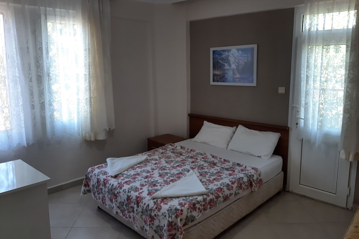 A bedroom with a bed, curtains, a painting, and a bedside table.