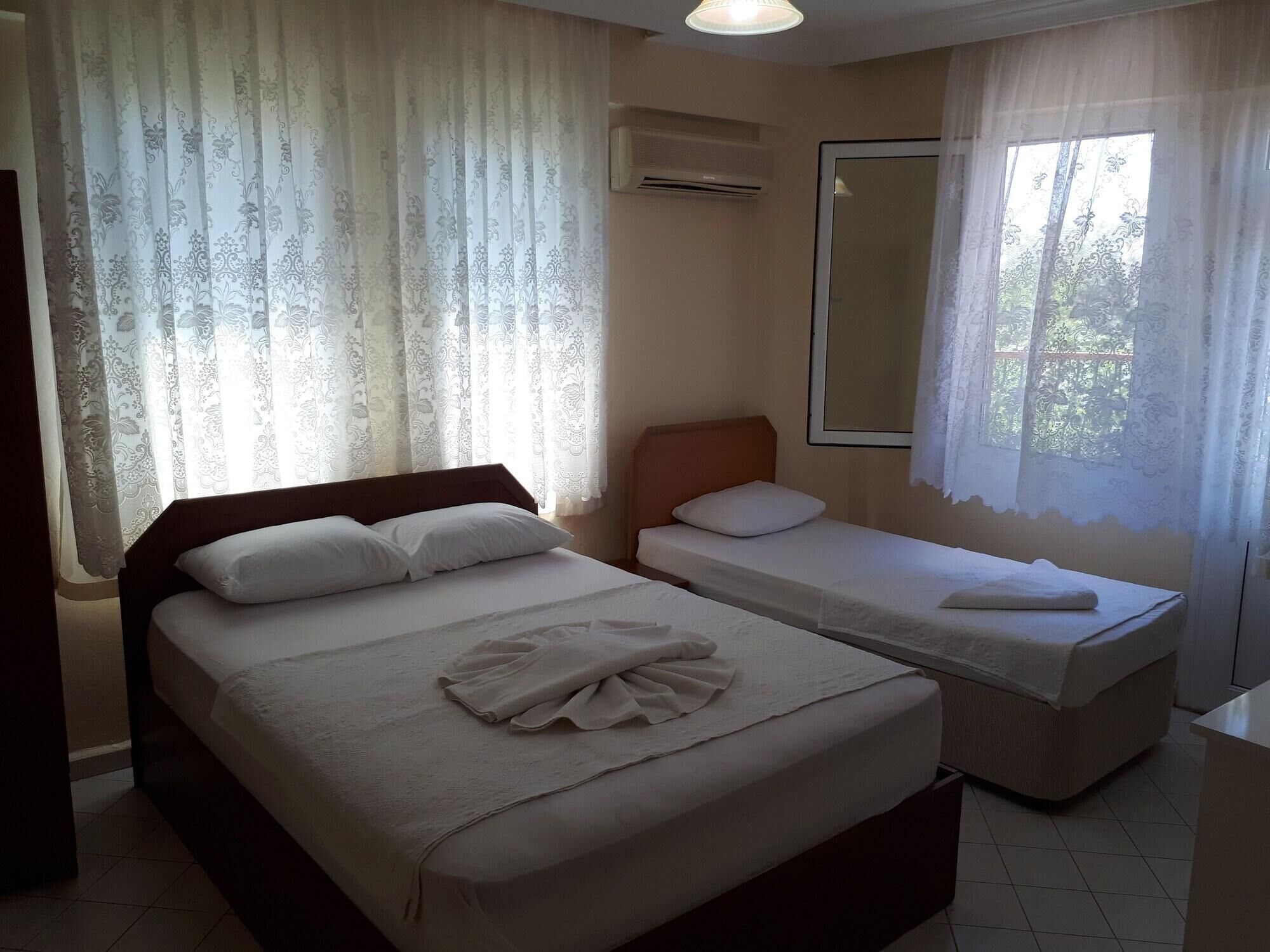 A hotel room with two beds, a large window with curtains, a mirror, and an air conditioning unit.