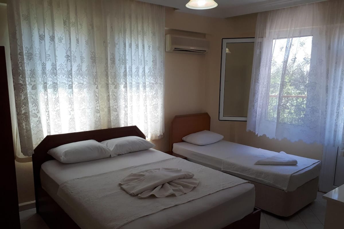 A hotel room with two beds, a large window with curtains, a mirror, and an air conditioning unit.