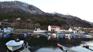 A harbor with boats docked, a white building with a red roof, and mountains in the background. - Vikedal Vertshus (Vindafjord)