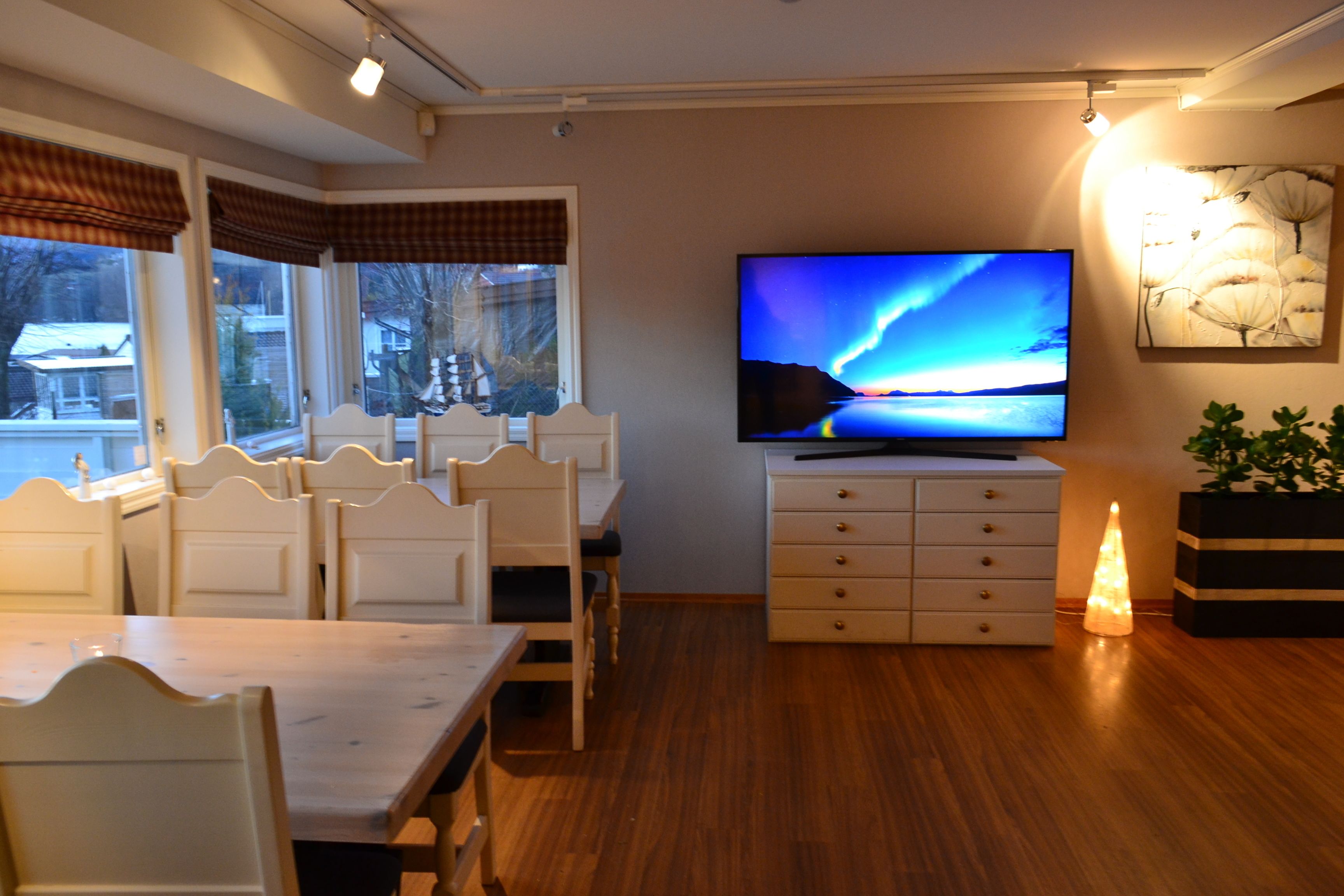 A dining area with a wooden table and chairs, a television on a dresser, and a plant.