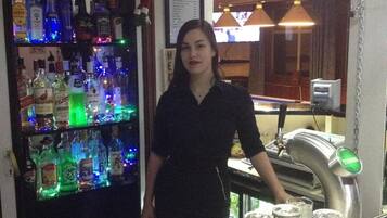 A bar area with a variety of liquor bottles, a bar counter, and a person standing behind the counter.