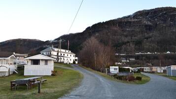 A gravel road leading to a cluster of white mobile homes with a large building in the background.