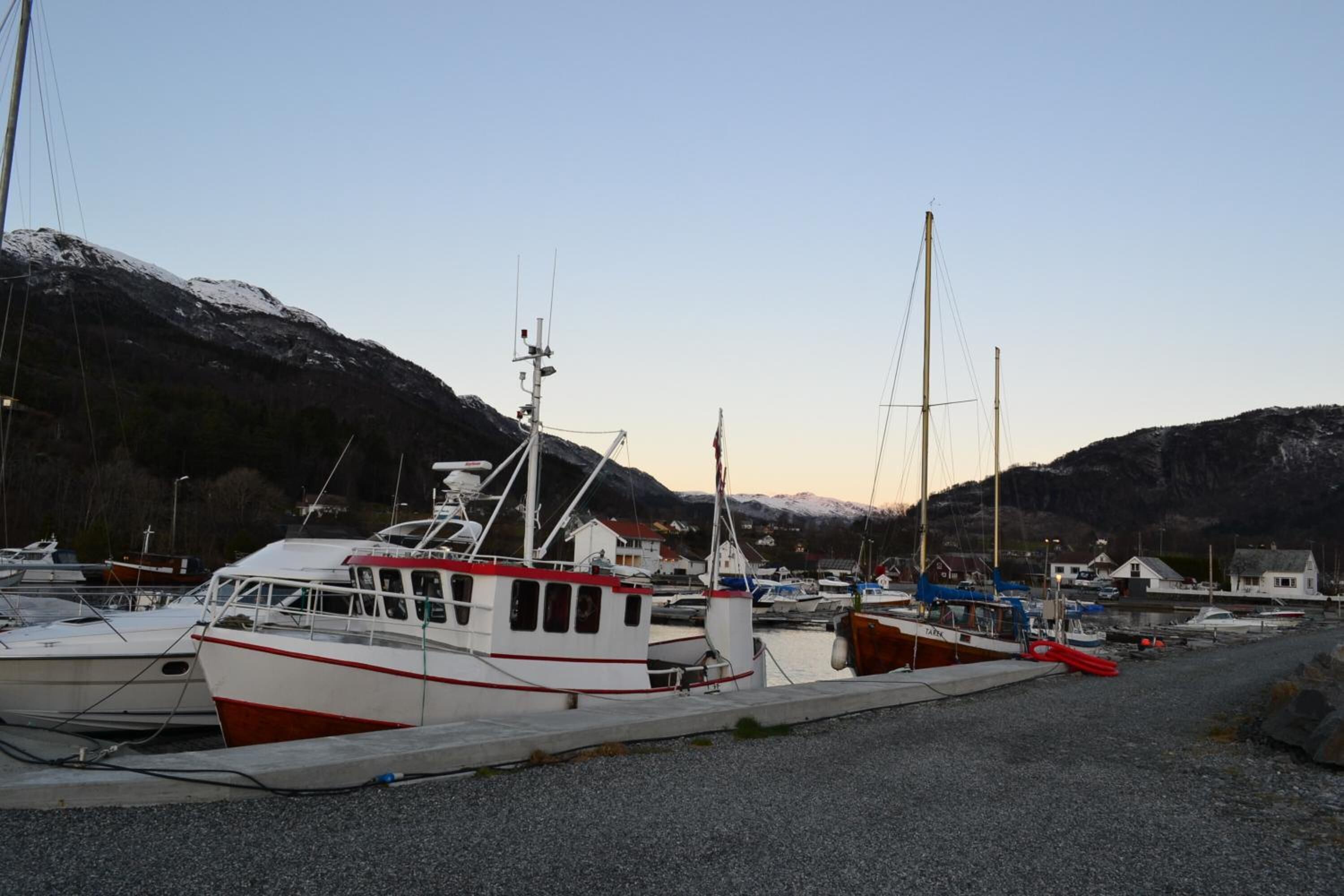 Uma marina com vários barcos atracados, cercada por montanhas e casas.
