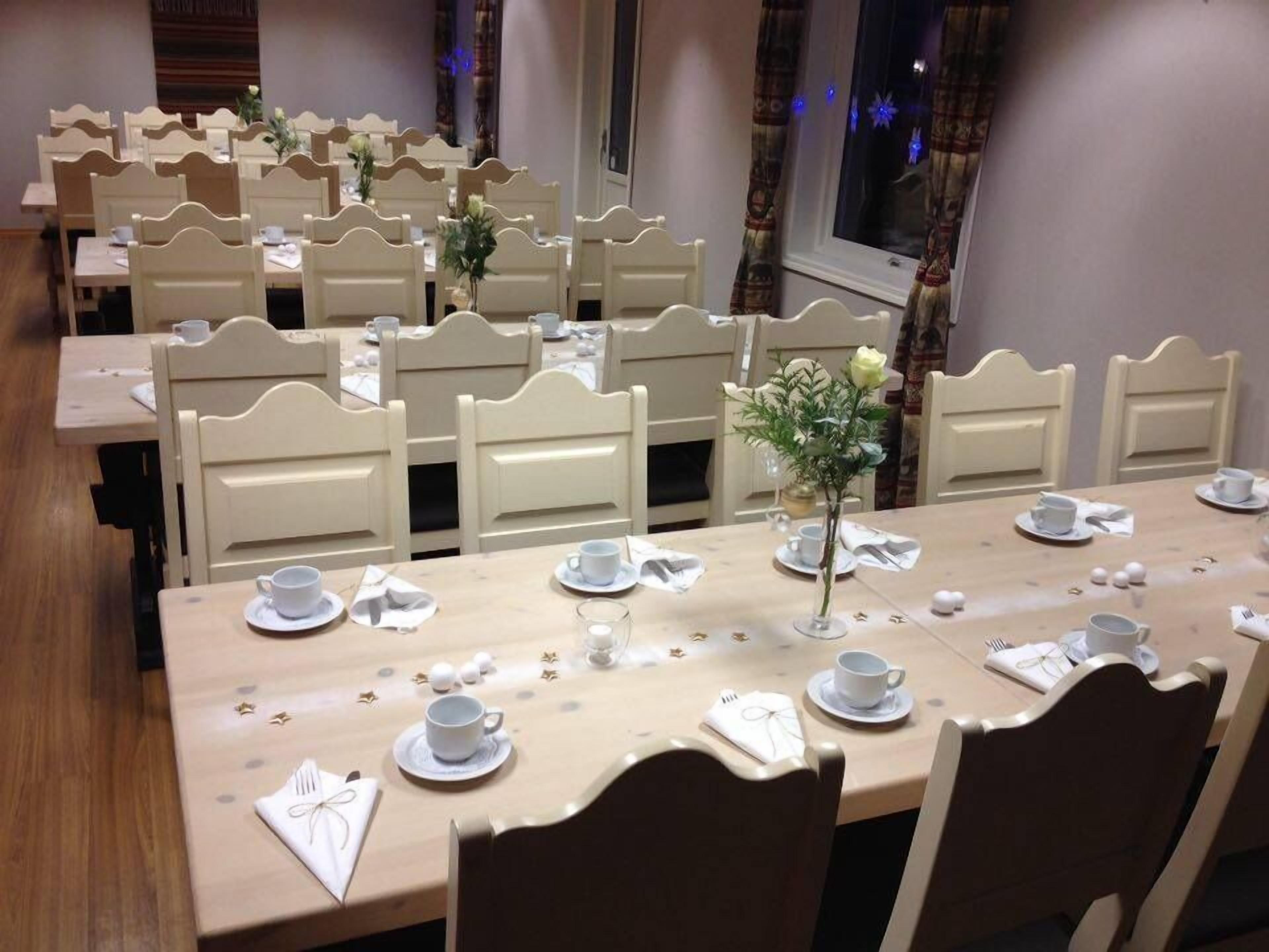 A dining area with multiple tables and chairs, each set with white tableware and a small vase of flowers.