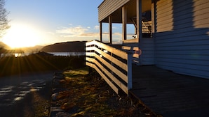 A wooden building with a porch overlooking a body of water and hills. - Vikedal Vertshus (Vindafjord)