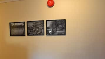 A room with a wooden floor, two chairs, a small table with a book, and three black-and-white framed pictures on the wall.